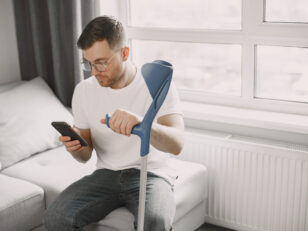 Young man with walking stick talk by phone indoors